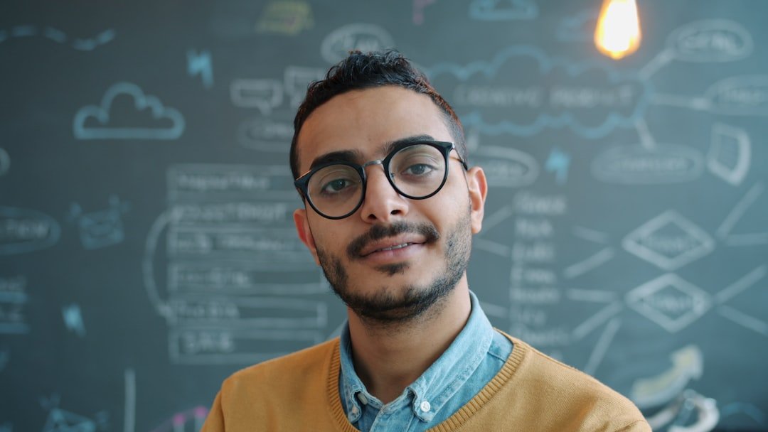 Man wearing glasses smiles in front of chalkboard