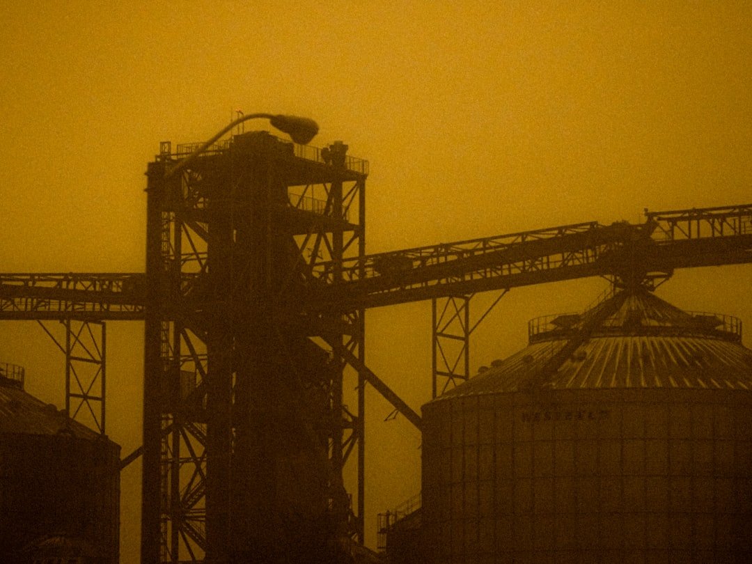 Industrial complex with silos and conveyor belts under hazy sky.